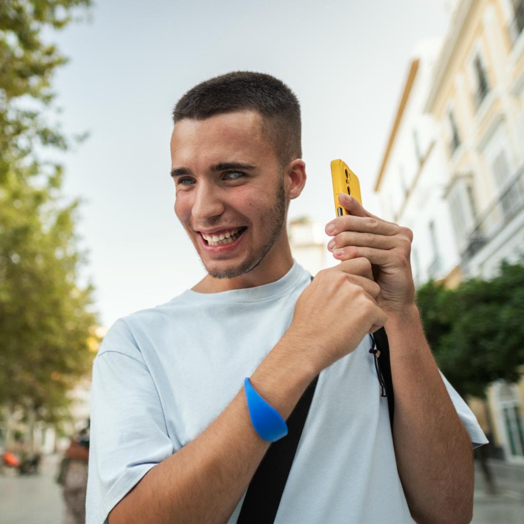 La photo montre un jeune homme aveugle, souriant, qui tient un téléphone portable. Il est en train d'écouter.
