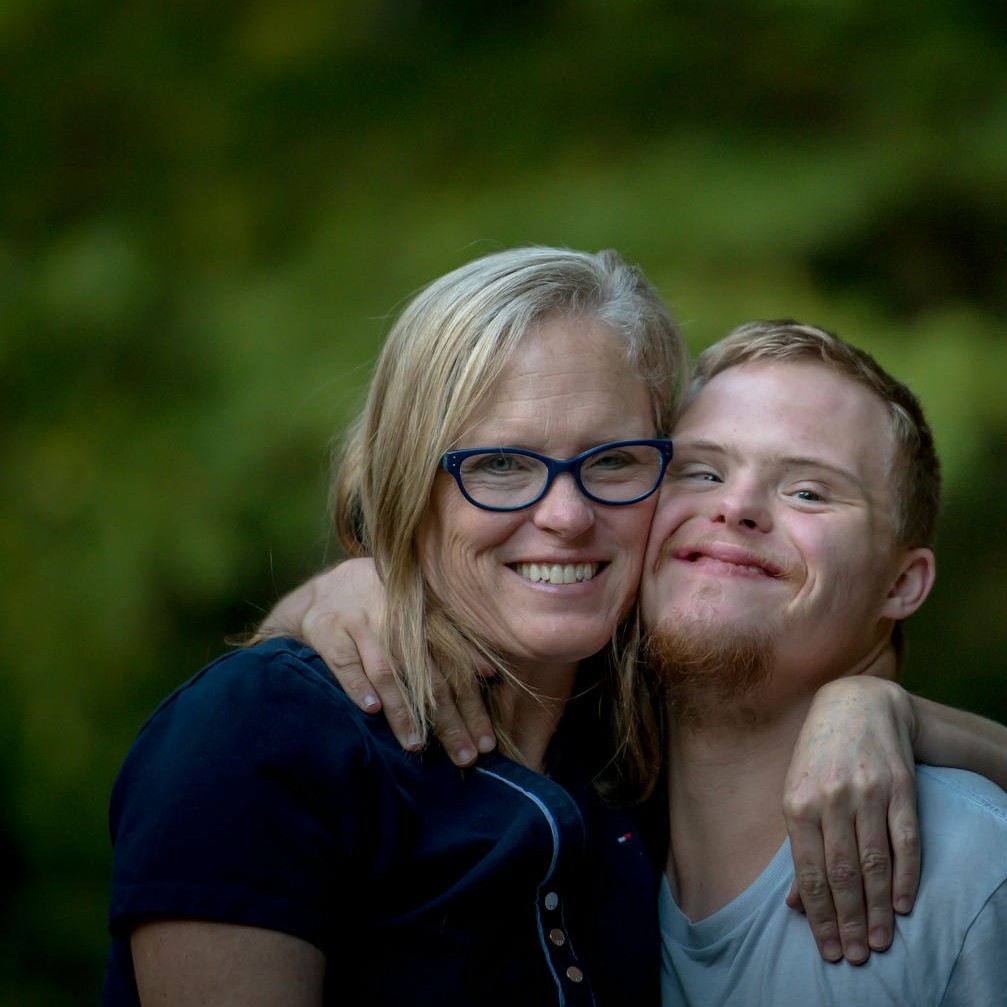 La photo montre des parents avec leur jeune fils porteur de la trisomie 21 ; ils rient et ont l'air heureux.