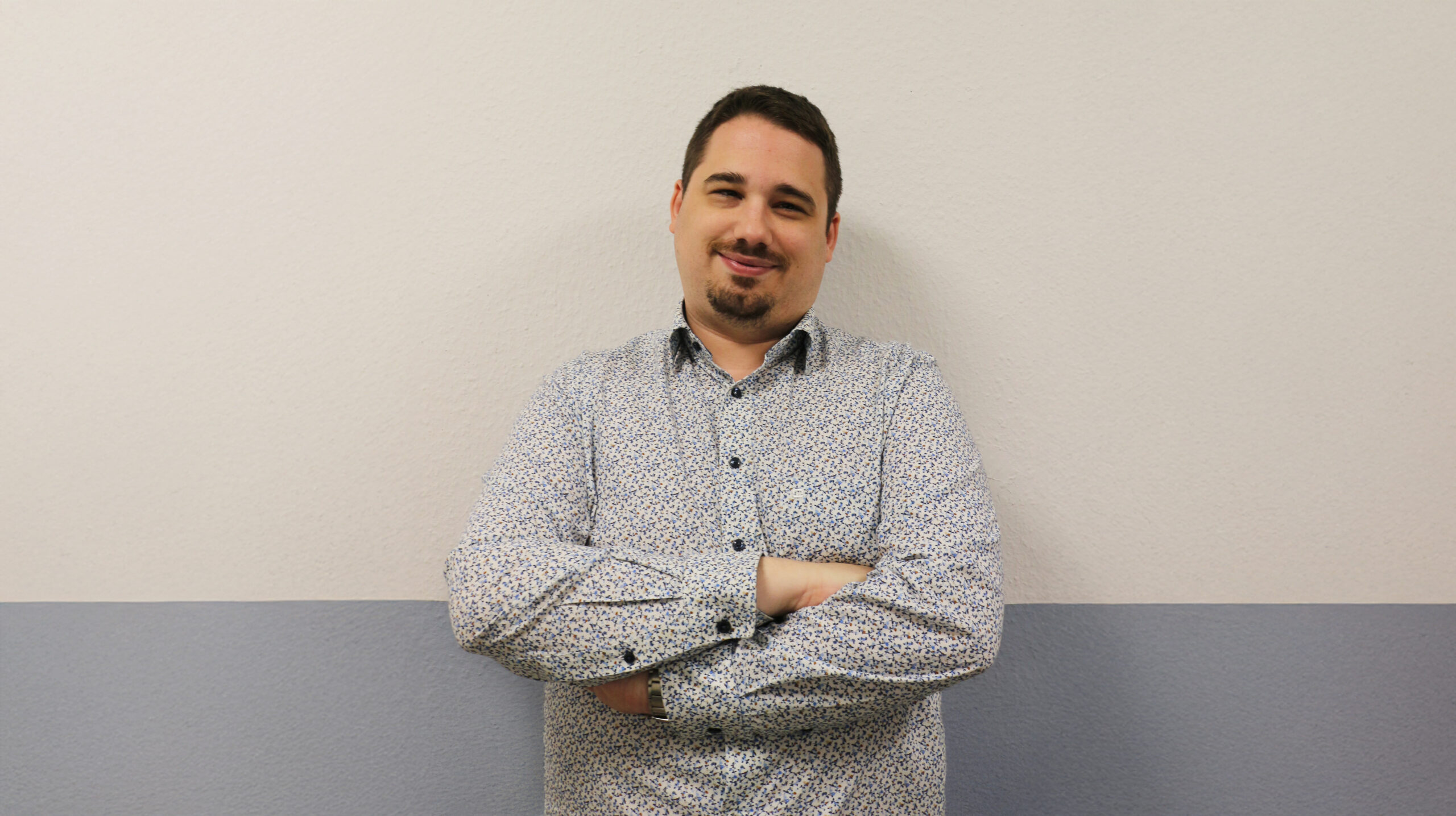 Frontalporträt von Sam Houblie, Personalchef bei Hornbach, lächelnd und mit verschränkten Armen