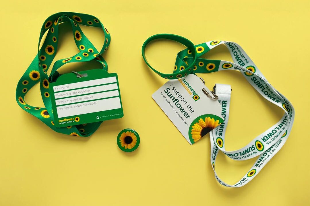 Zwei „Hidden Disabilities Sunflower“-Lanyards in Grün und Weiß mit Abzeichen und Pins mit Sonnenblumen.