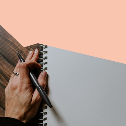 Sur la photo, on voit la main d'une personne tenant un stylo et, à côté, un bloc-notes vierge.