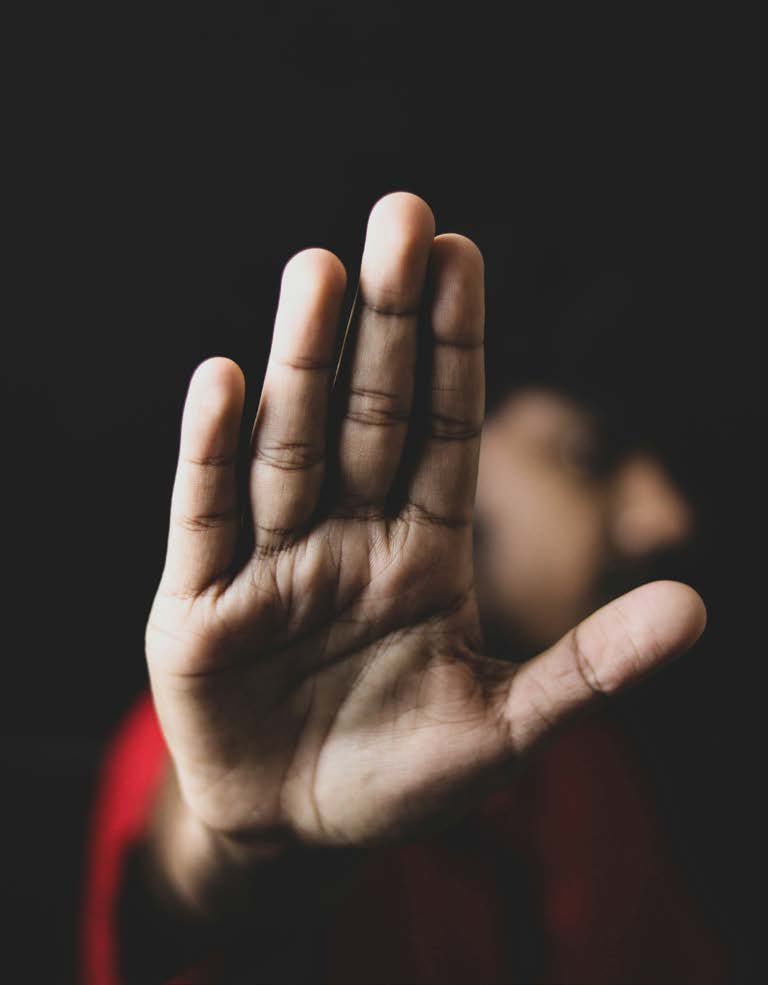 Vor schwarzem Hintergrund wird eine offene Hand als &bdquo;Stopp&ldquo;-Zeichen in die Kamera gehalten; die Person dahinter ist unscharf.