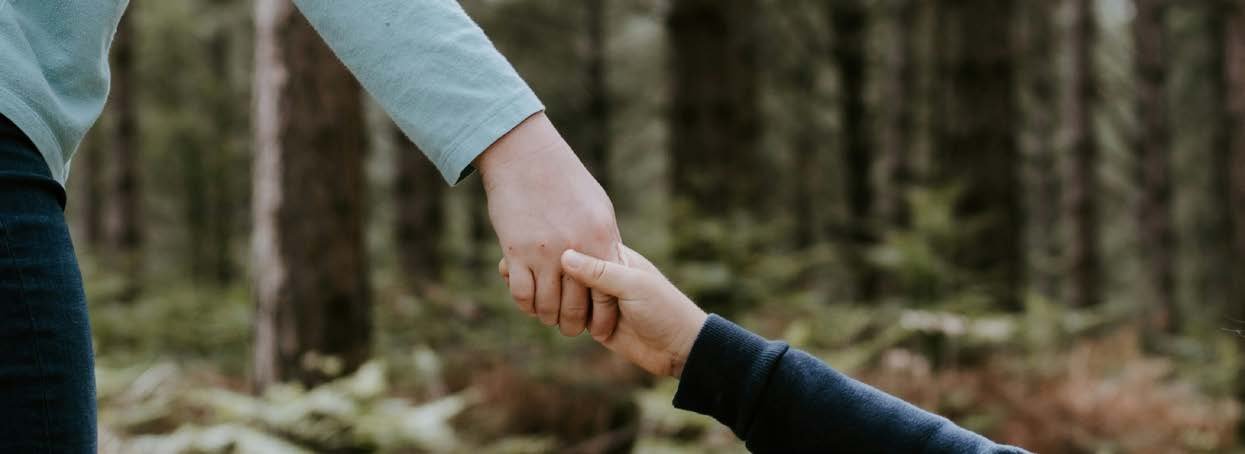In einem Wald zieht eine Person eine andere an der Hand; nur die Arme sind zu sehen.
